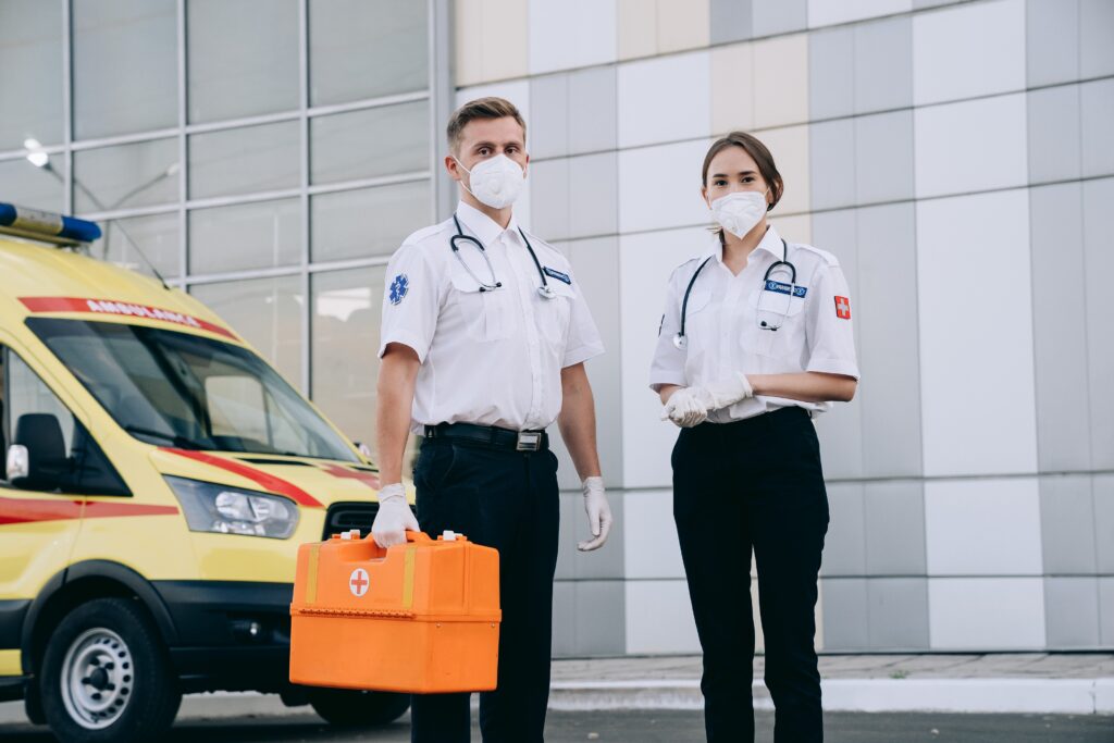 Dos paramédicos uniformados y con tapabocas, frente una ambulancia