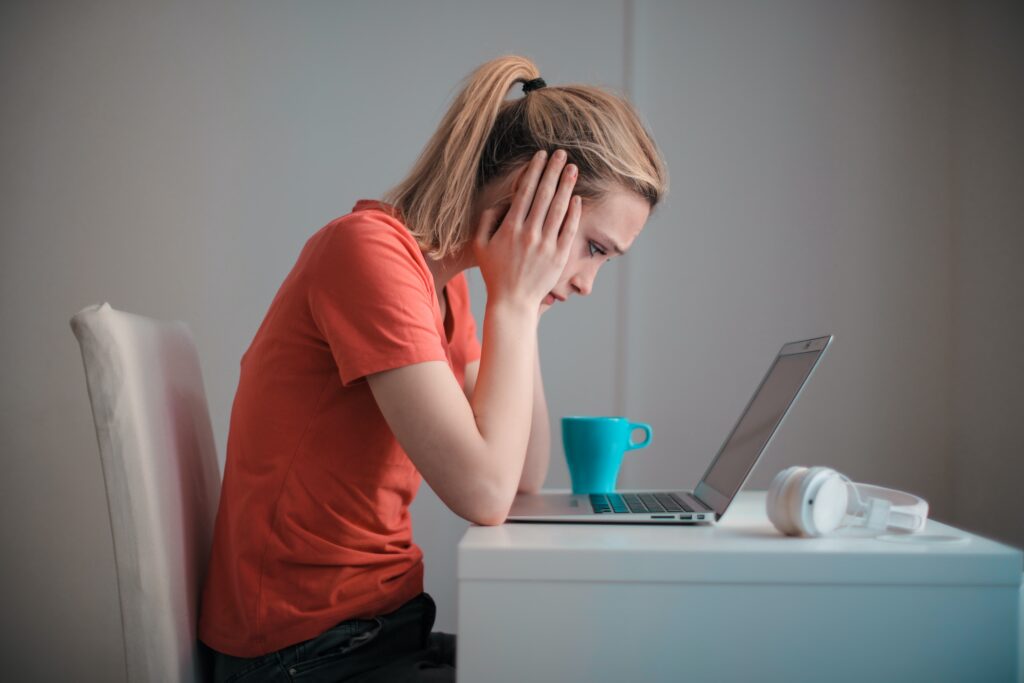 Mujer rubia preocupada con manos sobre su cara, mirando una laptop